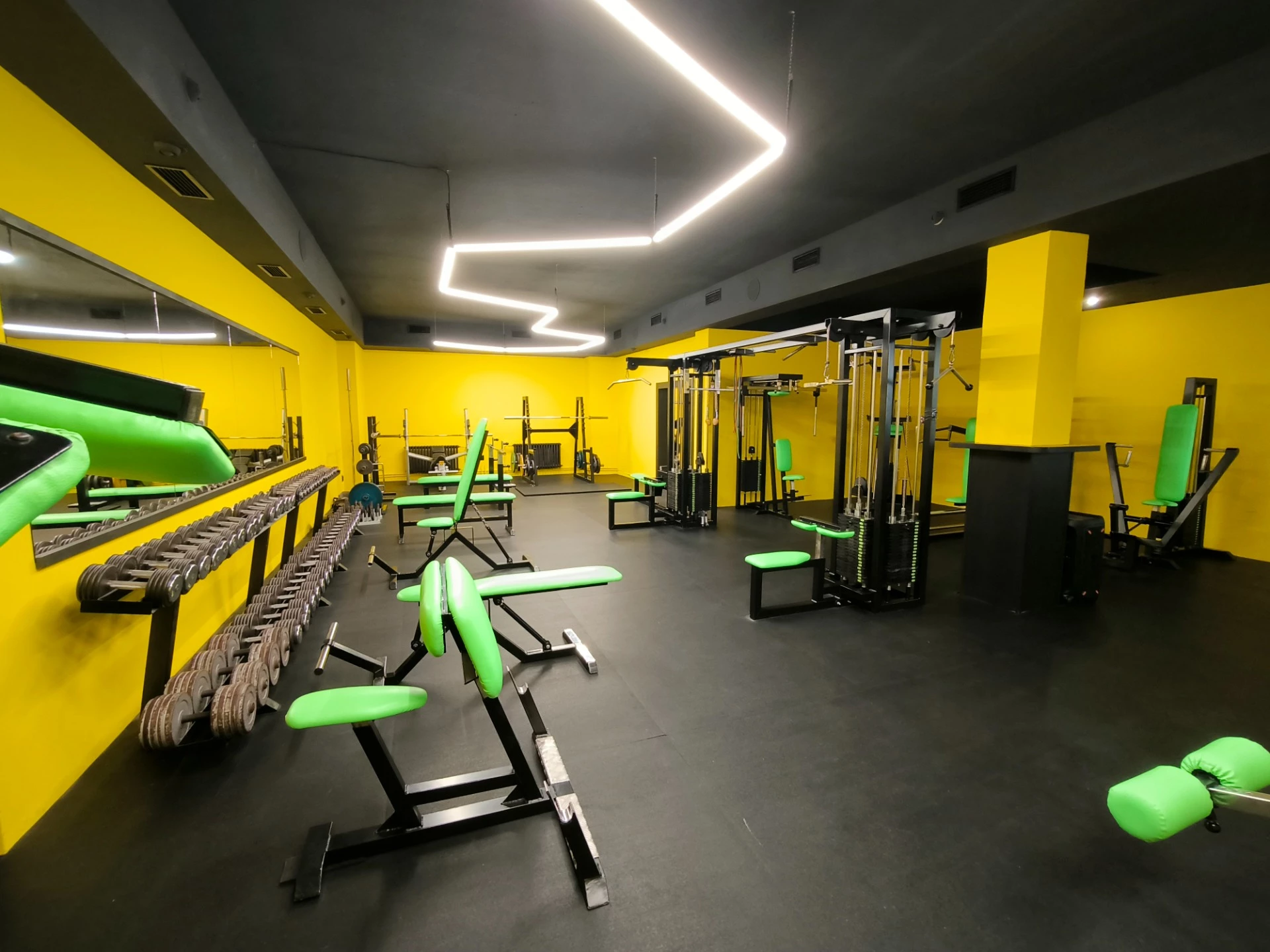 Černožlutý interiér Uran Gymu s činkami, lavicemi a posilovacími stroji